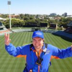 A man on the Adelaide Oval roof climb wearing a harness and smiling